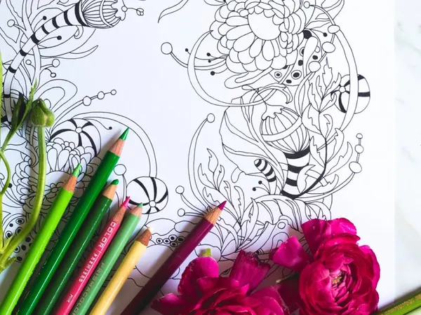 A coloring page, pencils and pink flowers on a marble table